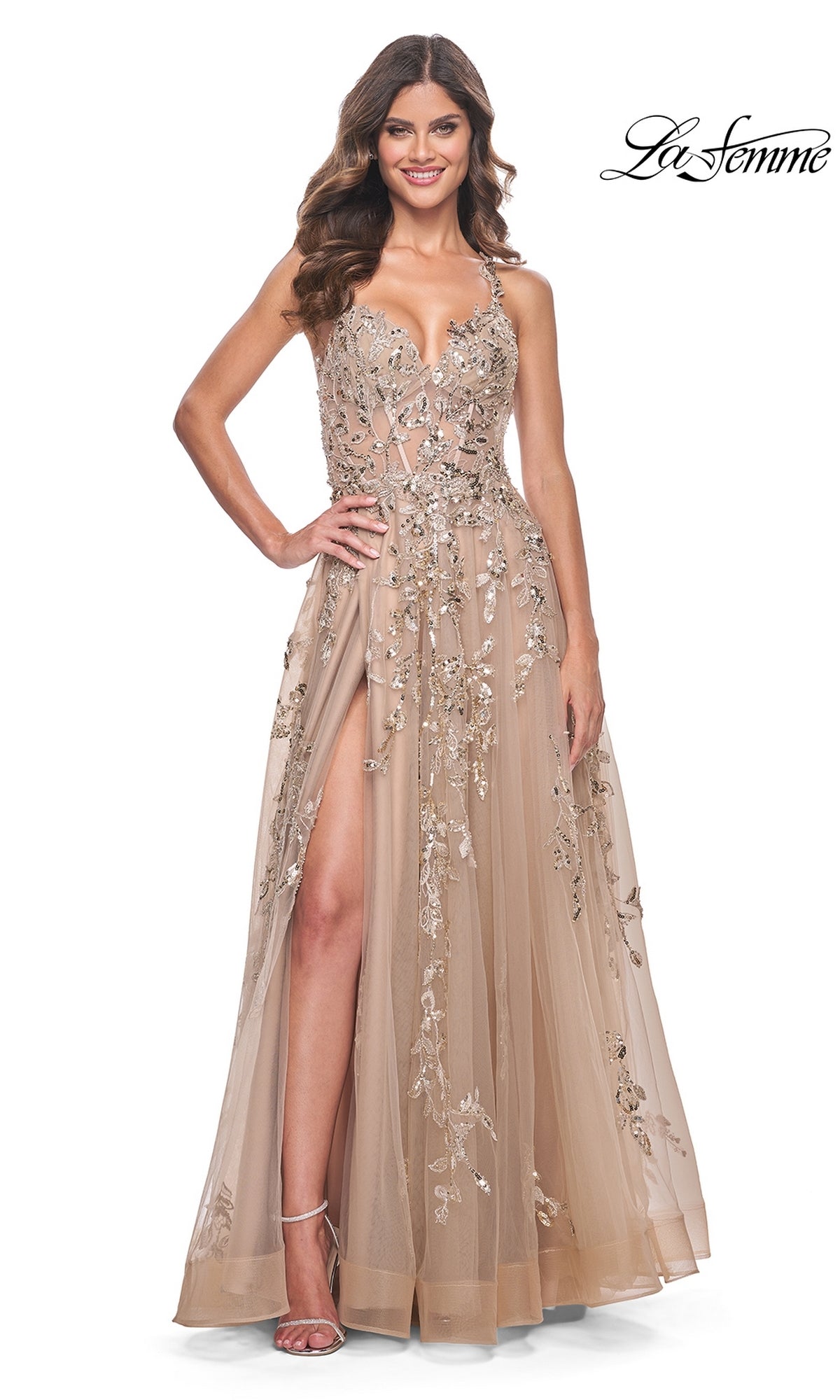 A woman wears the La Femme Sheer-Bodice Long Lace Prom Dress 32052—an elegant beige, floor-length gown with a sleeveless design, floral lace embellishments, thigh-high slit, and fitted A-line silhouette paired with strappy heels.